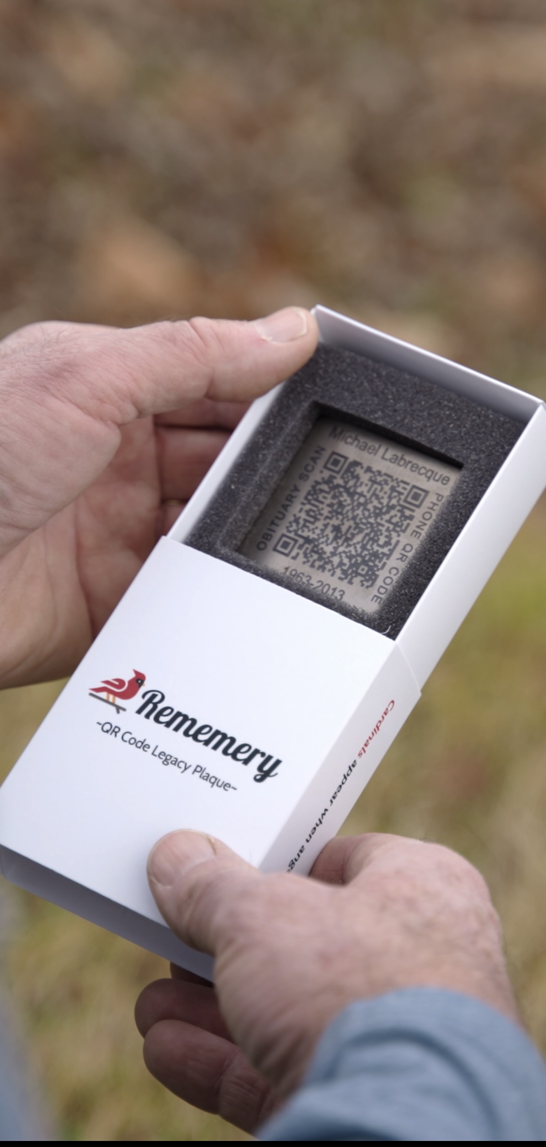 Rememery QR Code Legacy Plaque held in hands, showing titanium plaque in branded box